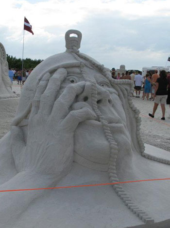 A sand sculpture of a man's head which appears to be sinking into the ground