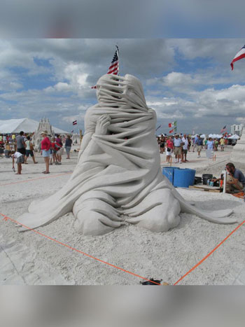Abstract sculpture made out of sand that appears to show two people wrapped together by a material