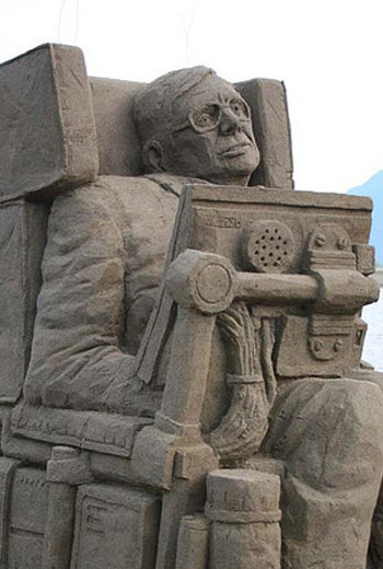 Sand sculpture of a disabled man, likely Stephen Hawking, sitting in his wheelchair 
