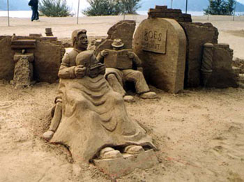 Sculpture made of sand depicting a man recieving a shave while another man reads in the corner