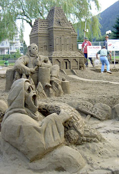 Abstract sand sculpture depicting two non-humans beings guarding a house