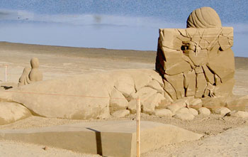 An image depicting the back side of a large sand sculpture with the ocean in the background