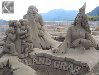 In this sand sculpture a large group of people huddled together as two large beings grab the land around them