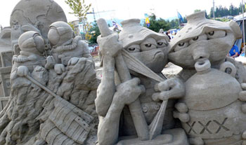 Non-human beings with three eyes are depicted in this abstract sand sculpture