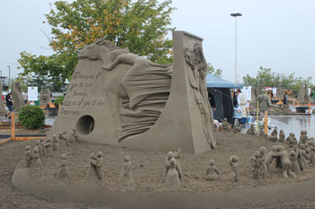 Large abstract sand sculpture of a ring of people surrounding a large statue depicting a man and a woman
